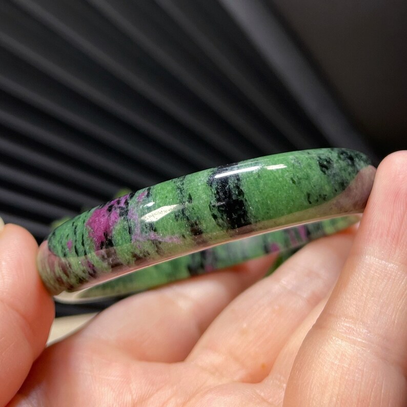 Puede incluir: Un brazalete de piedra preciosa verde, rosa y negro. El brazalete est&aacute; pulido y tiene una superficie lisa.