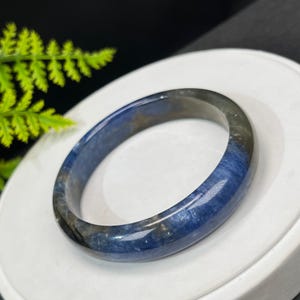 May include: A blue and gray gemstone bangle bracelet. The bracelet is made of a smooth, polished stone with a swirling pattern.