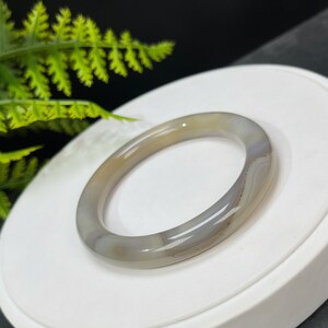 May include: A gray agate bangle bracelet with white and brown stripes. The bracelet is smooth and polished.