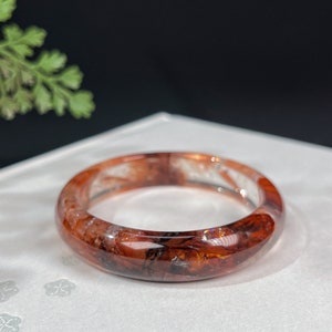 Op de afbeelding: Een rode en zwarte kristallen armband met een helder centrum. De armband is gemaakt van natuursteen en heeft een uniek, draaiend patroon.