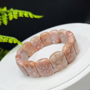 Könnte beinhalten: Ein rosafarbenes und weißes fossiles Korallenarmband mit rechteckiger Form. Das Armband besteht aus glatten, polierten Steinen mit einem natürlichen Muster.
