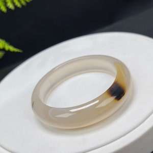 May include: A white agate bangle bracelet with brown and black markings. The bracelet is smooth and polished.