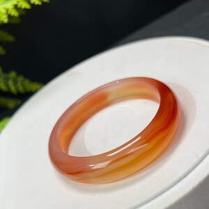May include: A red and orange agate bangle bracelet. The bracelet is made of polished stone and has a smooth, rounded surface.