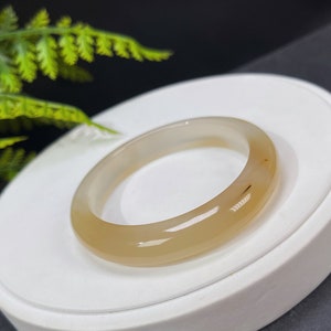 以下が含まれることがあります： 薄い茶色の瑪瑙のバングルブレスレット。ブレスレットは滑らかで磨かれており、控えめな光沢があります。