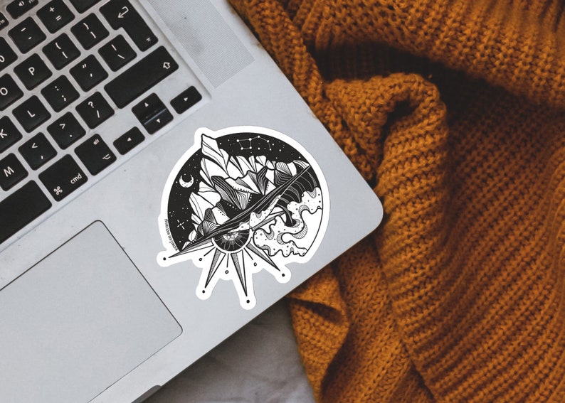 May include: Black and white sticker featuring a mountain range, a crescent moon, a sun with an eye, and waves. The sticker is on a silver laptop.