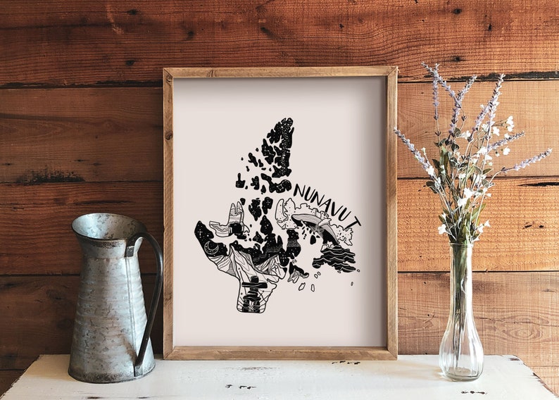 K&ouml;nnte beinhalten: Ein gerahmter Kunstdruck mit einer Schwarz-Wei&szlig;-Illustration der Region Nunavut in Kanada. Das Kunstwerk enth&auml;lt das Wort "NUNAVUT" und verschiedene grafische Elemente. Eine Metallkanne und eine Vase mit Blumen befinden sich im Vordergrund.