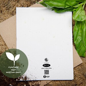 Pu&ograve; includere: Un biglietto di auguri con semi piantabili bianco con una busta di carta kraft, su una superficie di legno. La carta ha un logo circolare verde con un disegno a foglia e le parole "Plantable Seed Greeting Card". Sono visibili foglie di basilico fresco.