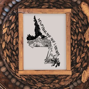 May include: A framed print with a black and white illustration of the Newfoundland and Labrador map. The artwork includes the text "NEWFOUNDLAND AND LABRADOR". The frame is made of wood. The print is displayed on a woven surface.