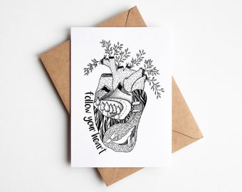 May include: A black and white illustration of a heart with a landscape design, including mountains, trees, and a whale. The words "follow your heart" are written on the left side of the heart. The card is placed on a brown envelope.