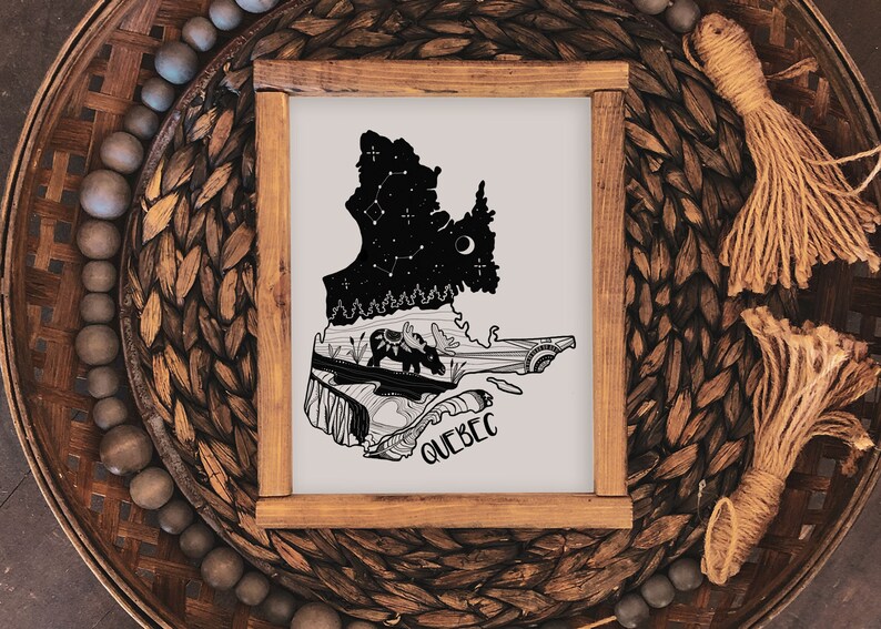 May include: A framed art print featuring the silhouette of the Quebec province, with a night sky design and moose illustration. The word "QUEBEC" is written at the bottom. The frame is made of wood and is set on a woven basket.