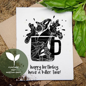Può includere: Biglietto di auguri con semi piantabili in bianco e nero con un disegno di orca all'interno di una tazza. Il biglietto recita "happy birthday, have a killer time!" su una superficie di legno.