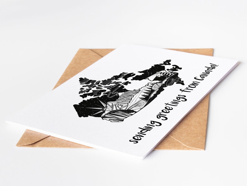 May include: A white greeting card with a black and white illustrated map of Canada, with the text "sending greetings from Canada!" The card is placed on a brown envelope, set against a white background.