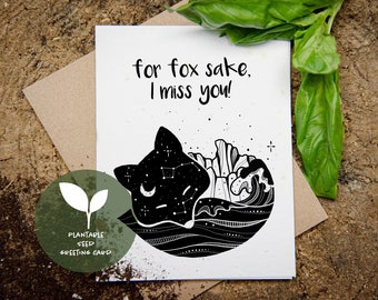 May include: A white greeting card with the text "for fox sake, I miss you!" and a black illustration of a fox with a starry sky design. The card is a plantable seed greeting card.
