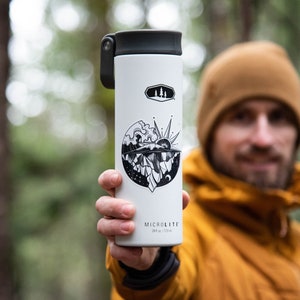 May include: White insulated water bottle with a black and white graphic of a mountain scene and a sun. The bottle has a black lid with a flip top and a black handle. The text "MICROLITE" is printed on the bottom of the bottle.