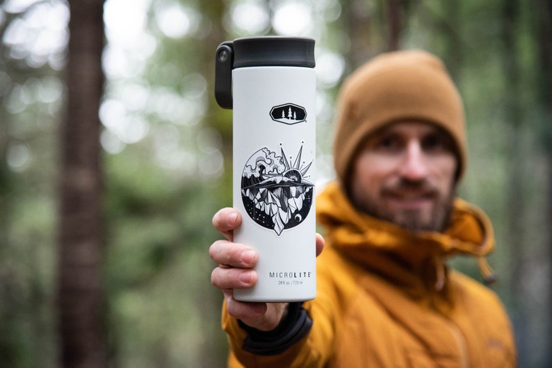 May include: White insulated water bottle with a black and white graphic of a mountain scene and a sun. The bottle has a black lid with a flip top and a black handle. The text "MICROLITE" is printed on the bottom of the bottle.