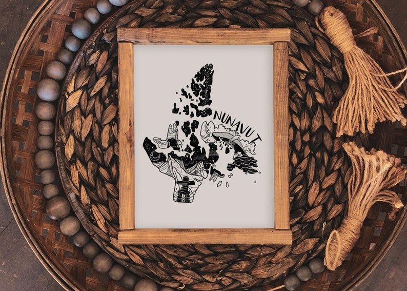 K&ouml;nnte beinhalten: Ein gerahmter Druck mit einer Schwarz-Wei&szlig;-Illustration der Region Nunavut. Das Kunstwerk ist vor einem hellen Hintergrund platziert und in Naturholz gerahmt. Der Druck wird auf einem gewebten Tablett mit dekorativen Elementen pr&auml;sentiert.