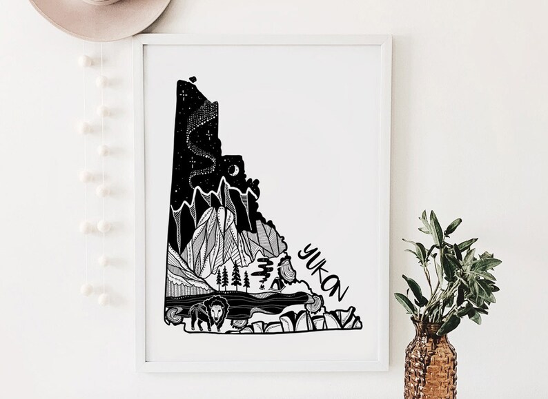 May include: Black and white art print of the Yukon territory. The artwork features a detailed illustration of mountains, trees, a bison, and the text "YUKON". The night sky is depicted with stars and a crescent moon. The print is framed in a white border.