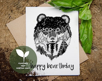 May include: A black and white plantable seed greeting card with a bear illustration. The bear's head features a starry sky, mountains, and a teepee design. The words "happy bearthday" are written below the bear.