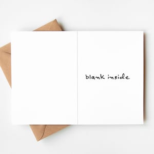 May include: A white greeting card with the words "blank inside" in black script, resting on a brown envelope. The card is open, revealing a blank interior. The envelope is partially visible, with its flap tucked in.