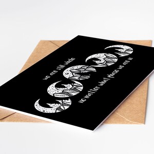 May include: A black greeting card with a white crescent moon design and the text "we are still whole no matter what phase we are in." The card is inside a brown envelope.