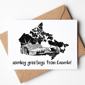 May include: A white greeting card with a black and white illustrated map of Canada, featuring mountains, trees, and a starry sky. The text "sending greetings from Canada!" is written in a handwritten style. The card is placed on a brown envelope.