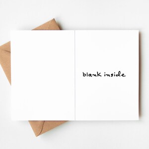 May include: A white greeting card with the words "blank inside" in black script, resting on a brown envelope. The card is open, revealing a blank interior. The envelope is a natural brown color.