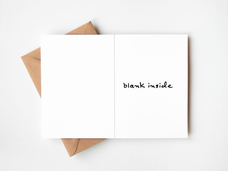 May include: A white greeting card with the words "blank inside" in black script, resting on a brown envelope. The card is open, revealing a blank interior. The envelope is a natural brown color.