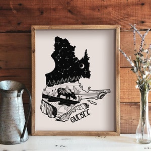 May include: A framed art print featuring a black and white illustration of the Quebec province. The artwork includes a starry night sky, a moose, and the word "QUEBEC". The print is displayed on a white surface with a metal pitcher and a vase of flowers.