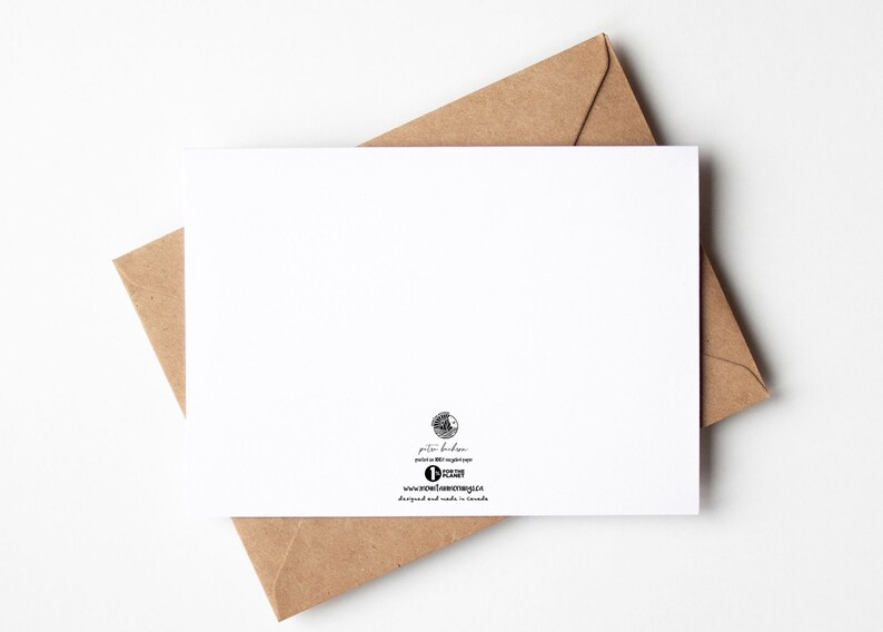 May include: A white greeting card with a brown envelope. The card is blank, with a small logo and text at the bottom. The envelope is a light brown color and partially visible behind the card.
