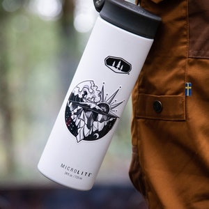 May include: White insulated water bottle with a black lid and a black and white sticker featuring a mountain range, a sun, and a wave. The sticker also includes a small moon and stars. The bottle has the text "MICROLITE 24 oz / 720 ml" printed on the bottom.
