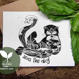 Può includere: Biglietto di auguri illustrato in bianco e nero con un design di lontra. Il corpo della lontra è riempito di immagini di montagne e oceani. Il testo "seas the day!" è sotto la lontra. Un cerchio verde con testo e una grafica di pianta è in basso a sinistra.