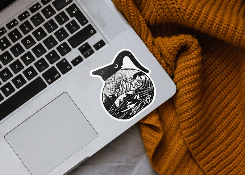 May include: Black and white sticker of a coffee pot with a mountain scene inside. The sticker is on a silver laptop.
