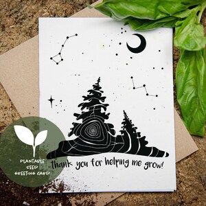 Può includere: Biglietto di auguri con semi piantabili in bianco e nero con un design di foresta e costellazioni. Il biglietto presenta il testo "thank you for helping me grow!" ed è accompagnato da una busta marrone e foglie verdi.