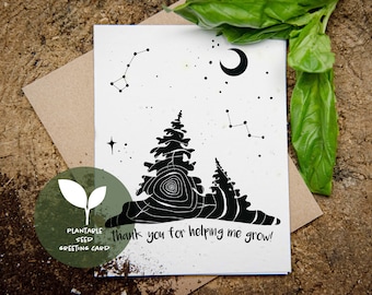 May include: A black and white plantable seed greeting card with a forest and constellation design. The card features the text "thank you for helping me grow!" and is accompanied by a brown envelope and green leaves.