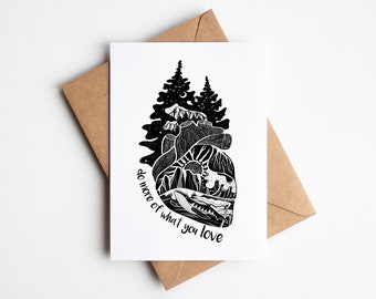May include: A black and white greeting card with a heart-shaped design featuring mountains, trees, and a whale. The card includes the text "do more of what you love" and is paired with a brown envelope.