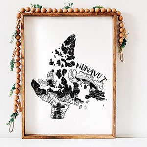 K&ouml;nnte beinhalten: Ein gerahmter Schwarz-Wei&szlig;-Druck der Nunavut-Karte. Die Karte ist eine detaillierte Illustration des kanadischen Territoriums, mit dem Wort "NUNAVUT" auf dem Bild. Der Rahmen ist aus Holz und mit Holzperlen und Gr&uuml;nzeug verziert.