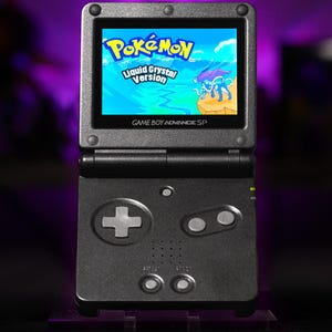 May include: A black Game Boy Advance SP handheld gaming console with a clamshell design. The screen displays the title screen for Pokémon Liquid Crystal Version, featuring the legendary Pokémon Suicune. The console has a D-pad, A and B buttons.