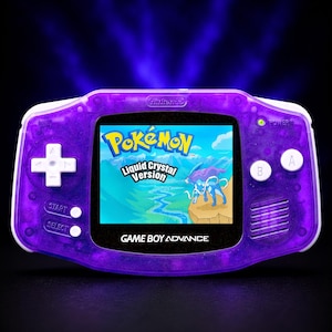 Könnte beinhalten: Ein transparent-lila Game Boy Advance Handheld-Konsolen, die das Spiel "Pokémon Liquid Crystal Version" anzeigt. Der Bildschirm zeigt eine blaue und grüne Landschaft mit zwei Pokémon-Charakteren. Die Konsole hat weiße Knöpfe und einen schwarzen Bildschirmrand.