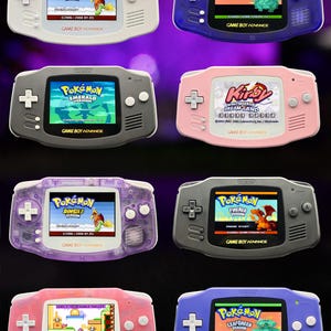 Op de afbeelding: Acht Game Boy Advance handheld consoles in diverse kleuren, waaronder wit, doorschijnend blauw, grijs, roze en paars. Elke console heeft een scherm waarop verschillende videospellen worden getoond, zoals Pokémon ShinyGold, LeafGreen, Emerald, FireRed en Kirby.