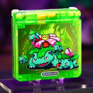 May include: A lime green translucent handheld gaming console featuring a pixel art graphic of Venusaur and Bulbasaur on the front cover. The device has a rectangular shape with a hinge at the top and a silver Nintendo logo centered at the bottom.