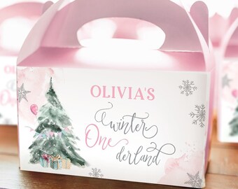May include: Pink party favor box with a handle, featuring a watercolor Christmas tree, snowflakes, and the text "Olivia's Winter One derland." The box has a pink top and a white front with a watercolor design.