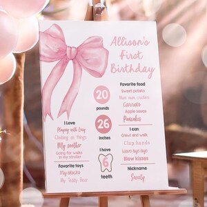 May include: A pink and white first birthday sign with a large pink bow at the top. The sign lists the child's age, weight, height, favorite foods, and activities. The text on the sign reads "Allison's First Birthday".