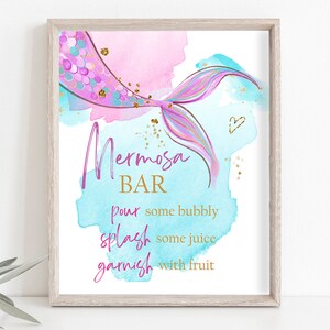 May include: A printable sign with a mermaid tail design and the text "Mermosa Bar" in pink and gold lettering. The sign instructs to "pour some bubbly, splash some juice, garnish with fruit".