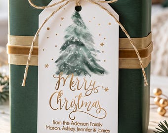 May include: A rectangular gift box wrapped in dark green paper with a gold velvet ribbon. A white gift tag is tied with twine, featuring a watercolor pine tree, gold stars, and the text Merry Christmas from the Aderson Family, Mason, Ashley, Jennifer & James.