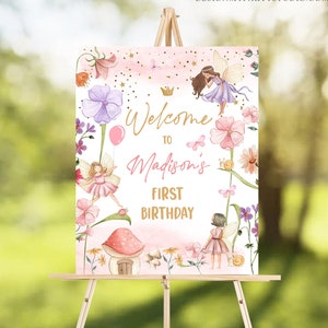 May include: Welcome to Madison's First Birthday sign with a pink and white background featuring fairies, flowers, and a mushroom house. The sign has a gold crown and gold lettering.