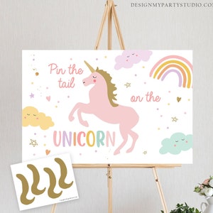 Pode incluir: Um tabuleiro de jogo branco com um unic&oacute;rnio rosa, um arco-&iacute;ris e nuvens. O texto no tabuleiro diz "Pin the tail on the unicorn". H&aacute; tr&ecirc;s caudas de unic&oacute;rnio douradas em uma folha de papel branca separada.