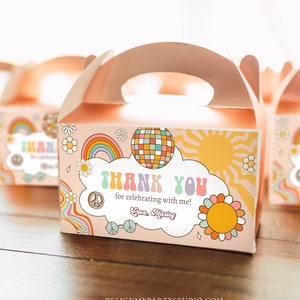 Può includere: Una scatola regalo rosa e arancione con un design a arcobaleno, segno di pace e sole. La scatola ha un manico e dice "Grazie per aver festeggiato con me! Con affetto, Marley".