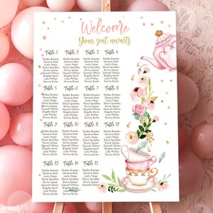 May include: A white welcome sign with pink floral and teacup illustrations, displayed on a wooden easel. The sign lists table numbers and guest names, with the text "Welcome, Your seat awaits."