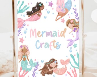 May include: A framed print with the words "Mermaid Crafts" surrounded by illustrations of mermaids in various colors. The mermaids have pink, blue, and purple tails, with brown, black, and blonde hair. The frame is gold.