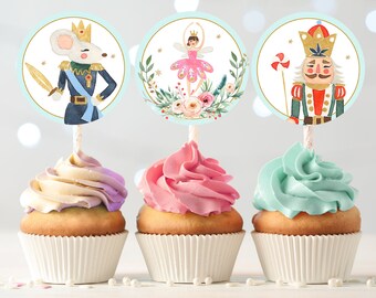 May include: Three cupcakes with decorative toppers featuring watercolor illustrations. The toppers depict a mouse soldier, a ballerina, and a nutcracker. Each cupcake has a different color frosting: lavender, pink, and teal. The cupcakes are in white paper liners.